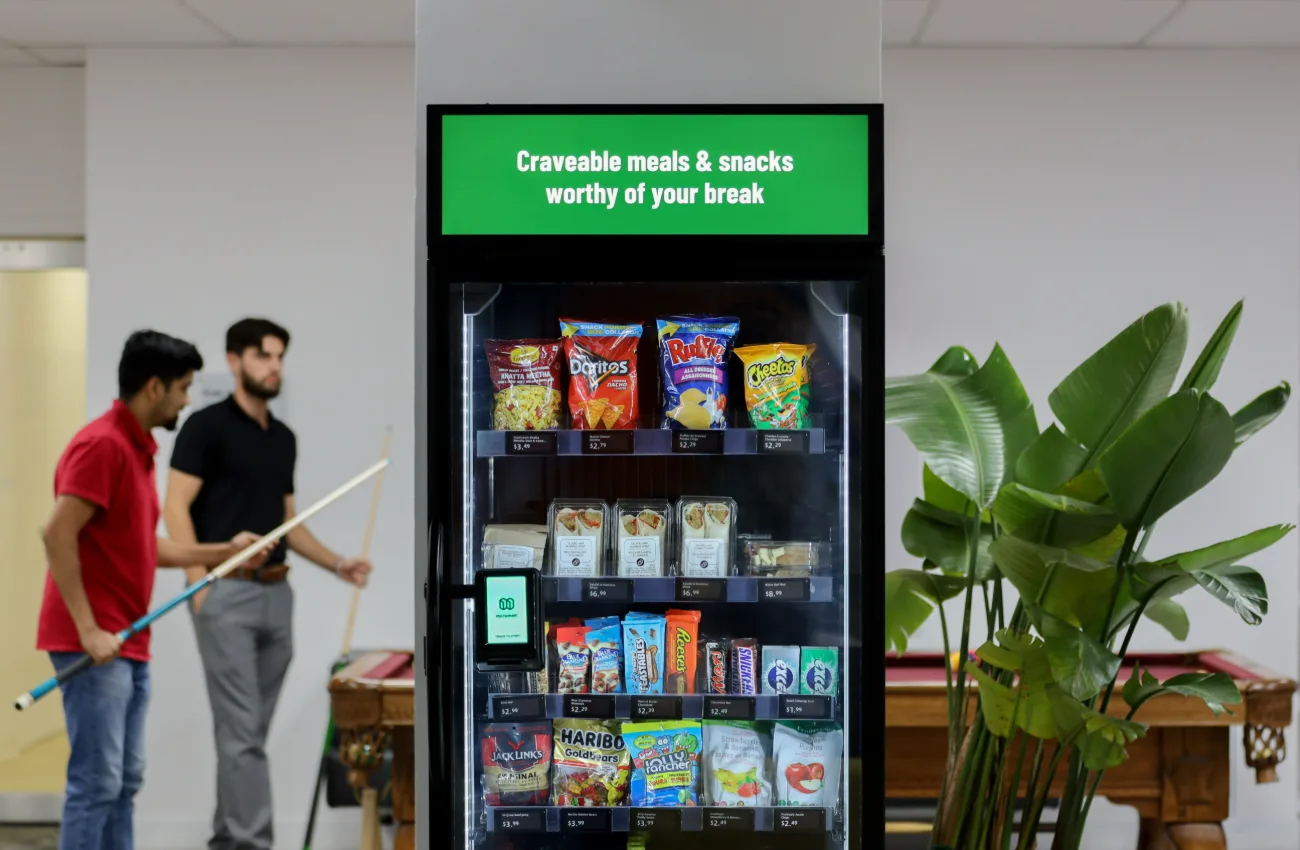 A smart vending machine installed in a workplace break room with a lit display above the cabinet